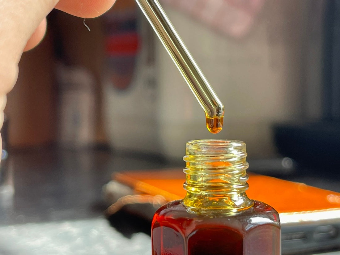 I’m holding a pipette with a drop of Oud oil dropping into a bottle with kitchen in the background