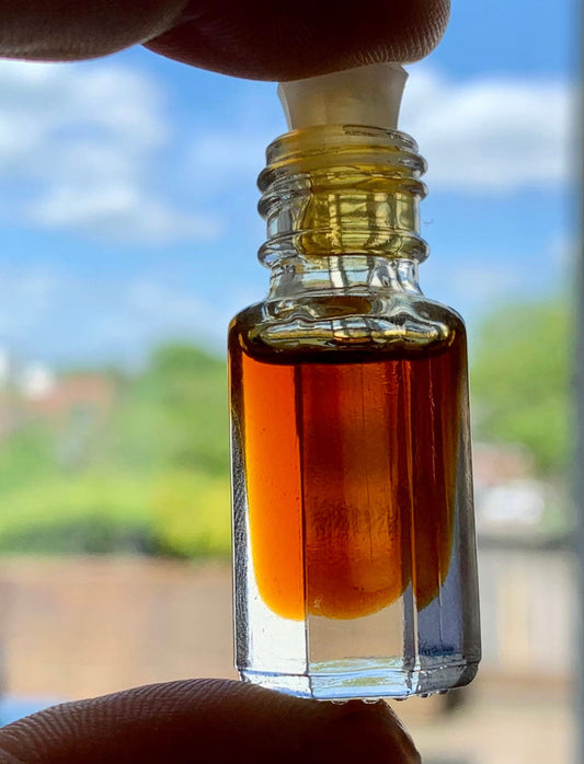 Man holding a bottle of wild oud oil with two fingers and blurred garden in the background