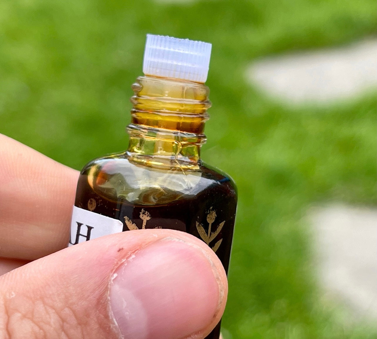 Man holding a big bottle of Kedah Oud oil with grass in the background