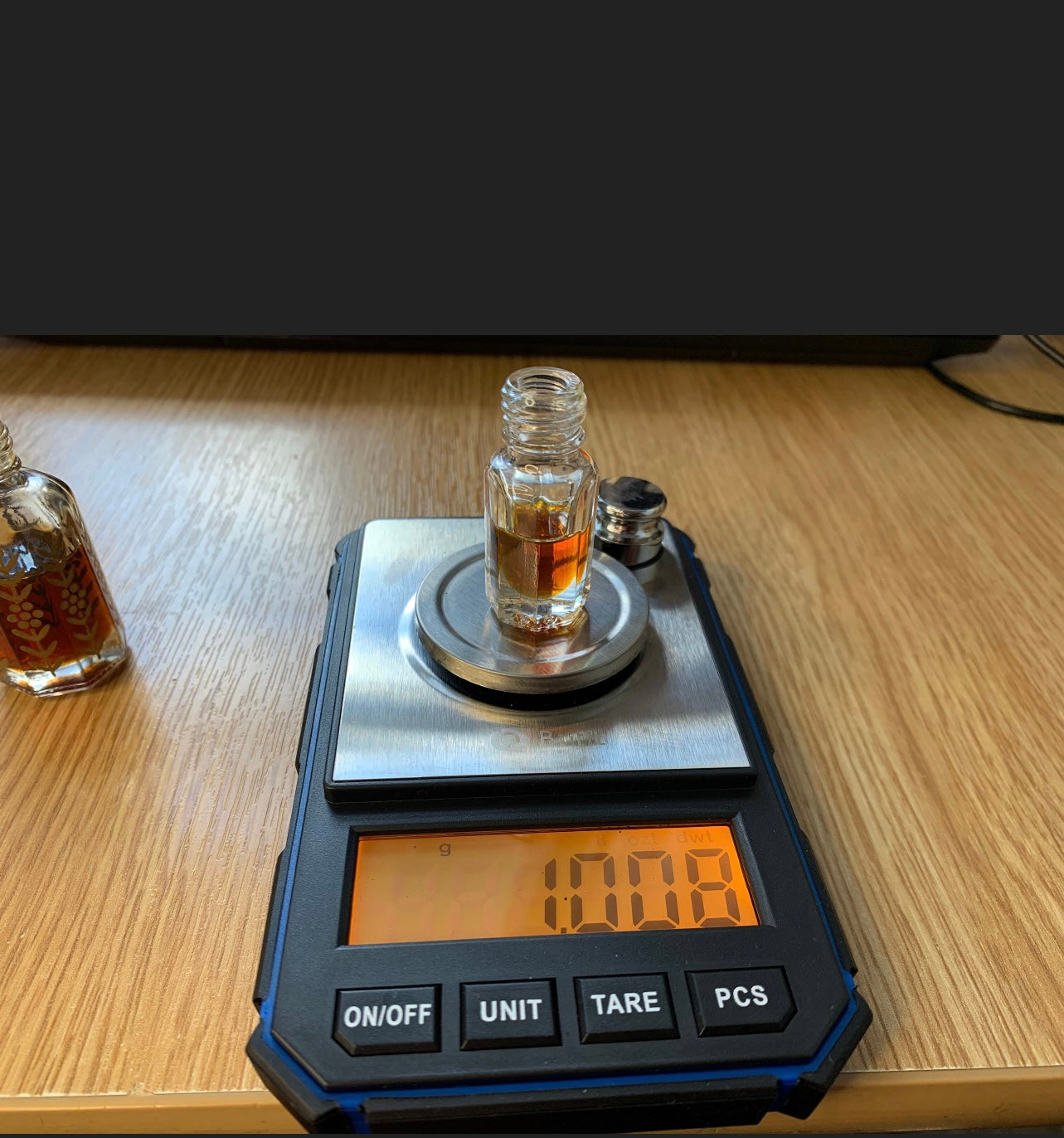 Weighing an Attar bottle of Oud oil on scales on a table 